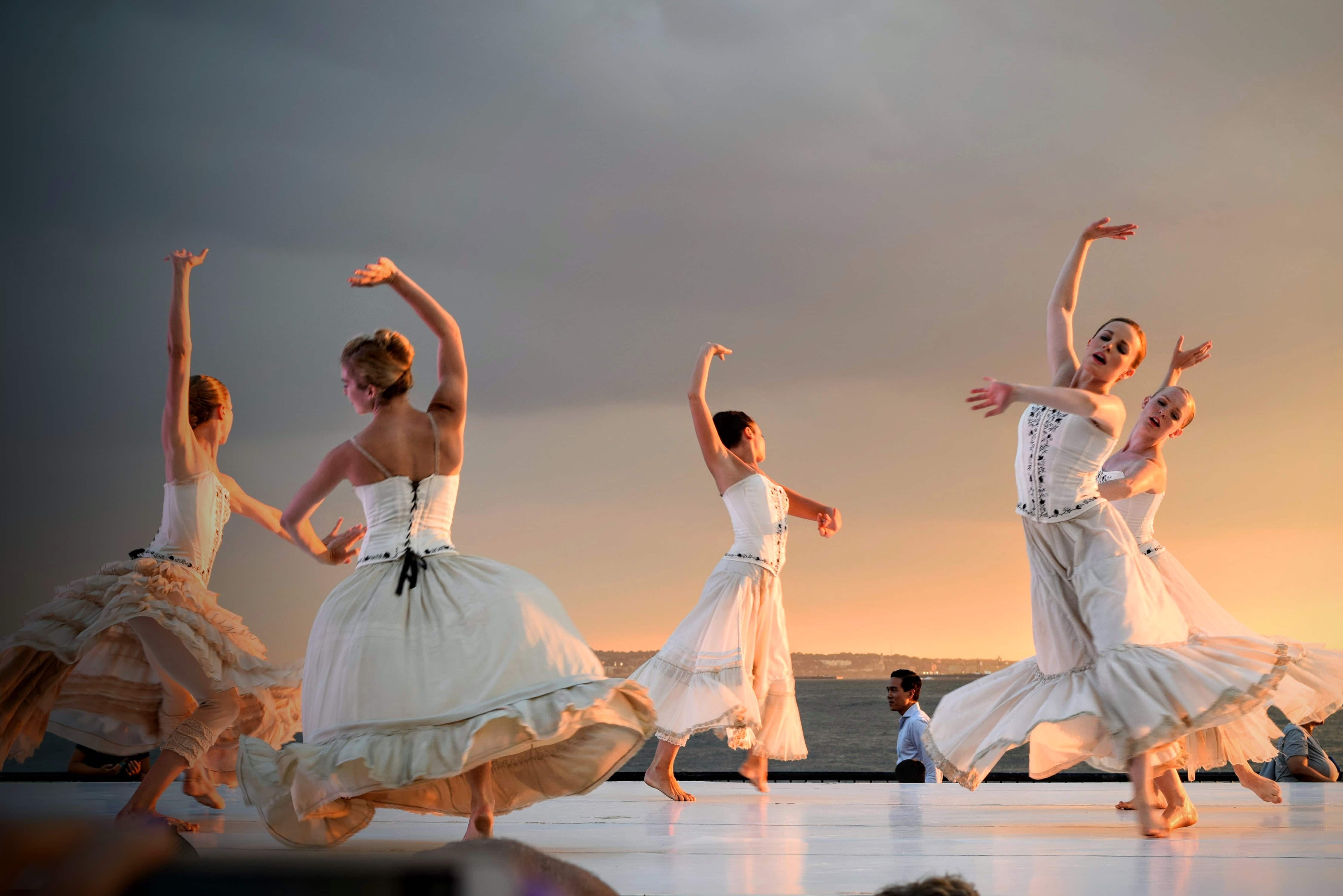 Dancers dressed in white on stage, with the sea in the background.