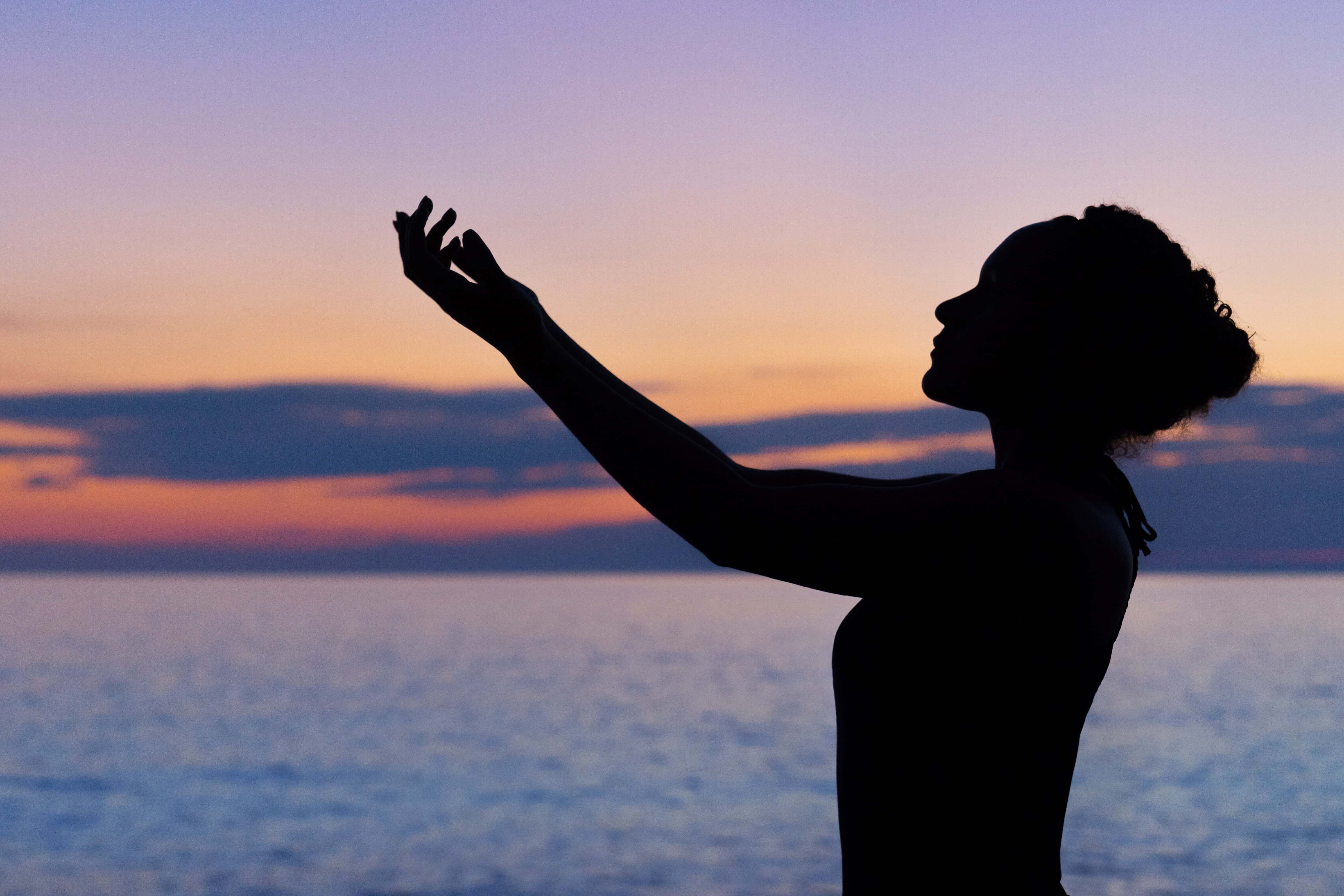 Silhouette of woman practising yoga in front of the sea.
