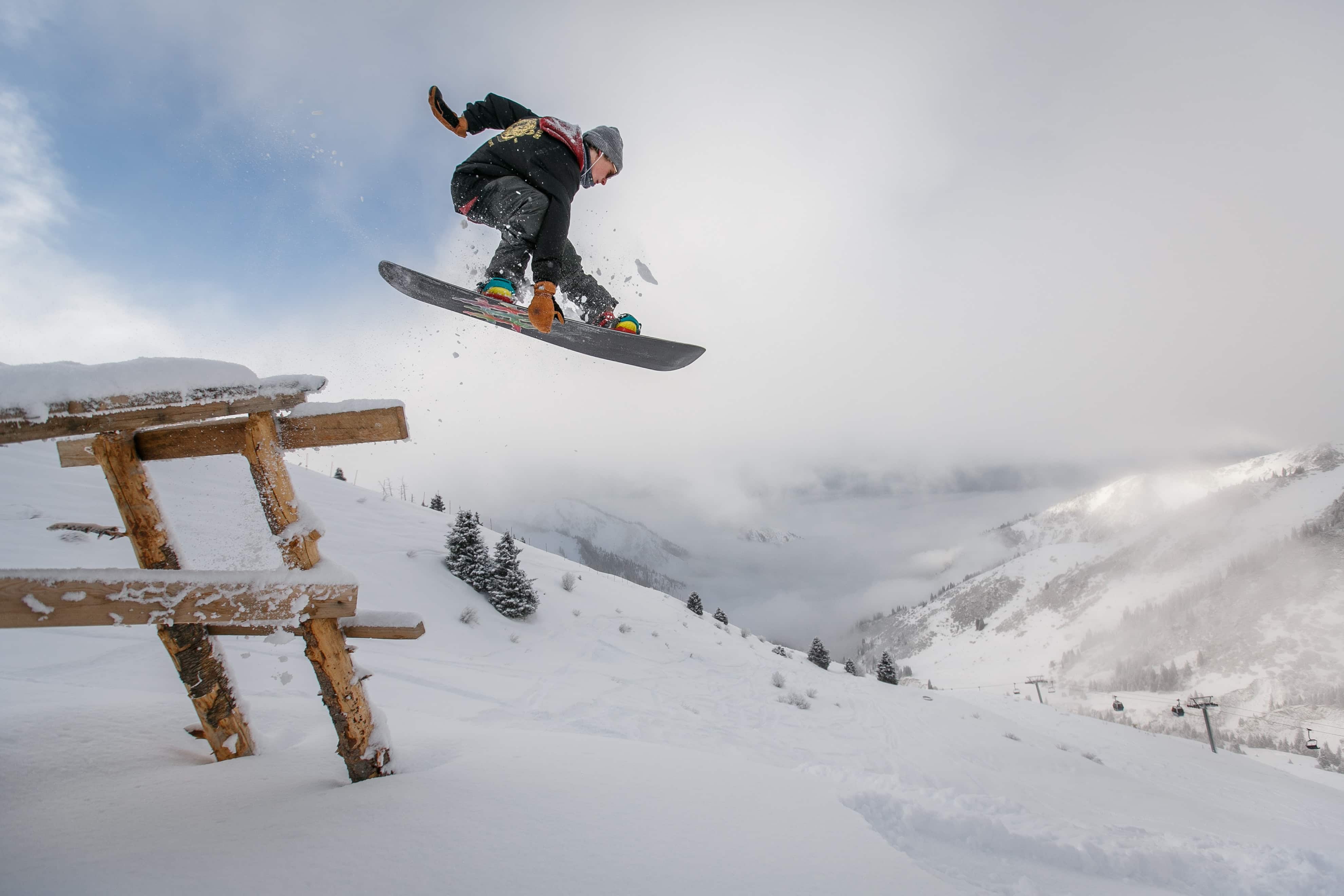 Snowboarder jumping over wooden bench in snow